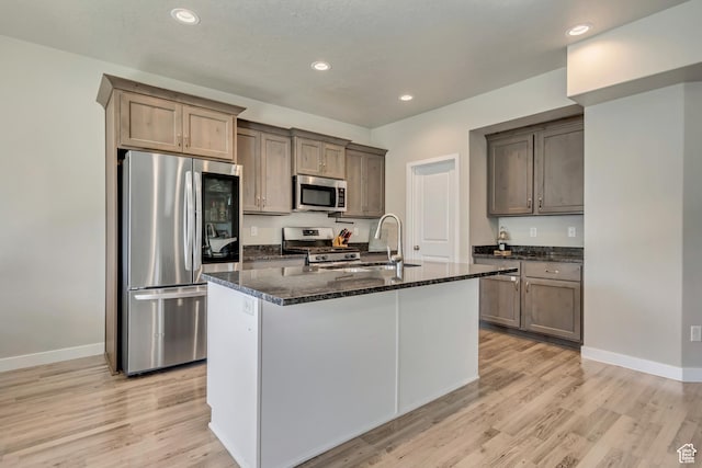 2466 S 2200 W, West Haven, UT 84401 - kitchen featuring appliances with stainless steel finishes, dark stone counters, light wood-style flooring, recessed lighting, and an island with sink