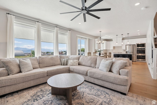 13321 S Split Oak Dr, Herriman, UT 84096 - living room featuring light wood-style flooring, a chandelier, a ceiling fan, recessed lighting, and a textured ceiling