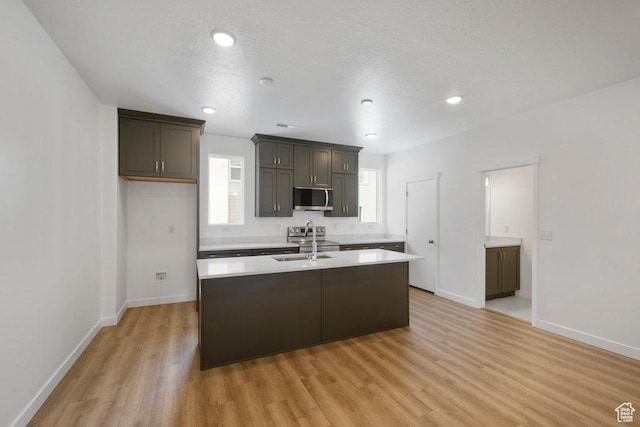 937 W Coalburn Way Unit 102, Murray, UT 84123 - kitchen with stainless steel appliances, light countertops, light wood-style flooring, a center island with sink, and baseboards