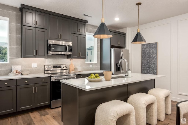 937 W Coalburn Way Unit 102, Murray, UT 84123 - kitchen with stainless steel appliances, a sink, wood finished floors, light countertops, and an island with sink
