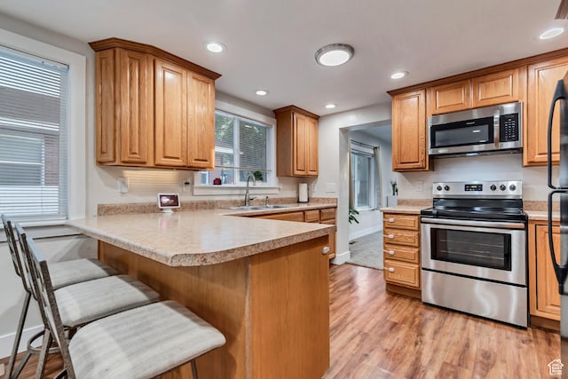 2867 S Cyprus Ln, Magna, UT 84044 - kitchen with appliances with stainless steel finishes, a sink, light wood-style flooring, a breakfast bar area, and a peninsula
