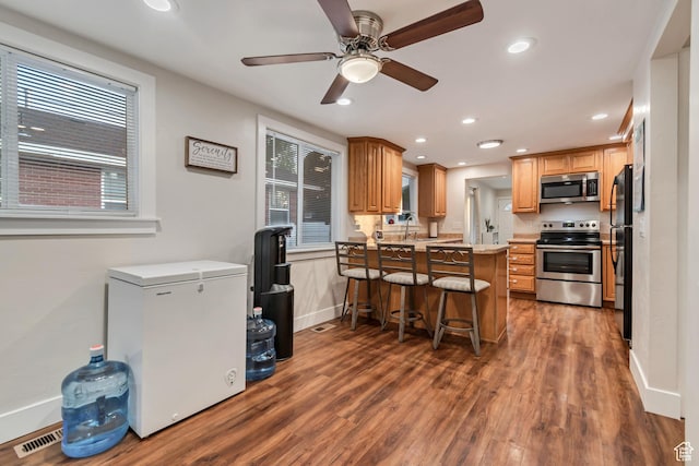 2867 S Cyprus Ln, Magna, UT 84044 - kitchen with appliances with stainless steel finishes, a peninsula, a breakfast bar, recessed lighting, and dark wood finished floors