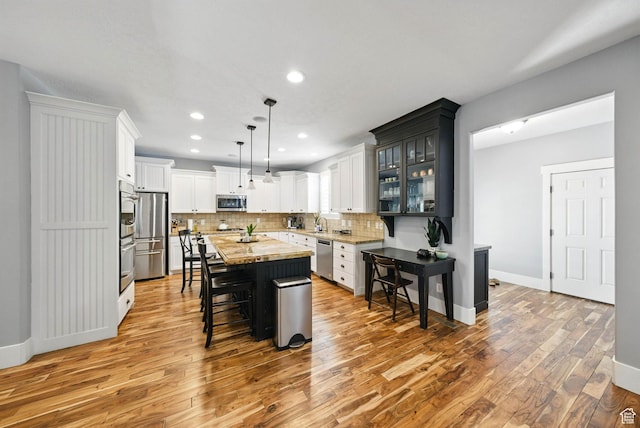 10416 S Vermillion Dr W, South Jordan, UT 84009 - kitchen with appliances with stainless steel finishes, light wood-style flooring, a breakfast bar, a kitchen island, and tasteful backsplash