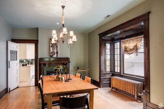 216 B St, Salt Lake City, UT 84103 - dining room featuring radiator heating unit, light wood-style floors, a chandelier, and a fireplace
