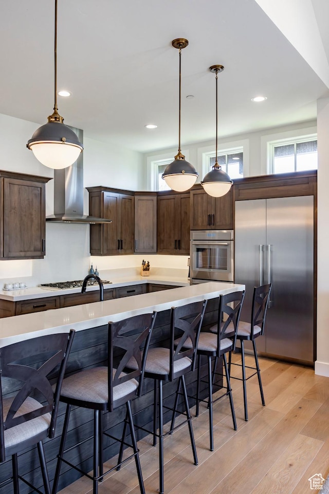 201 N Kings Peak Ct Unit Cp-23, Heber City, UT 84032 - kitchen with stainless steel appliances, dark brown cabinetry, wall chimney range hood, light countertops, and light wood-style floors