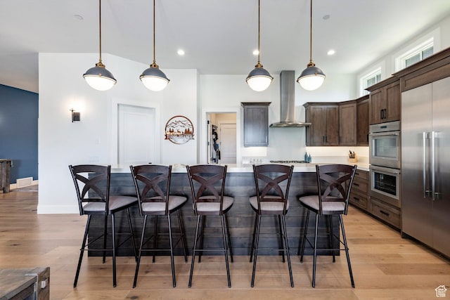 201 N Kings Peak Ct Unit Cp-23, Heber City, UT 84032 - kitchen featuring wall chimney range hood, appliances with stainless steel finishes, dark brown cabinets, light countertops, and a breakfast bar area