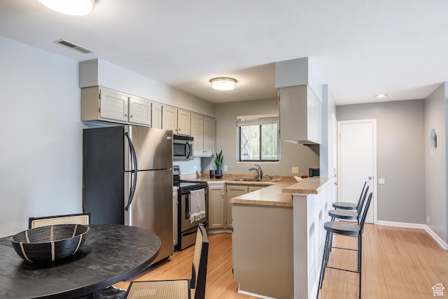 2660 E 3300 S Unit A-21, Salt Lake City, UT 84109 - kitchen with appliances with stainless steel finishes, a peninsula, light countertops, a kitchen breakfast bar, and light wood-style flooring