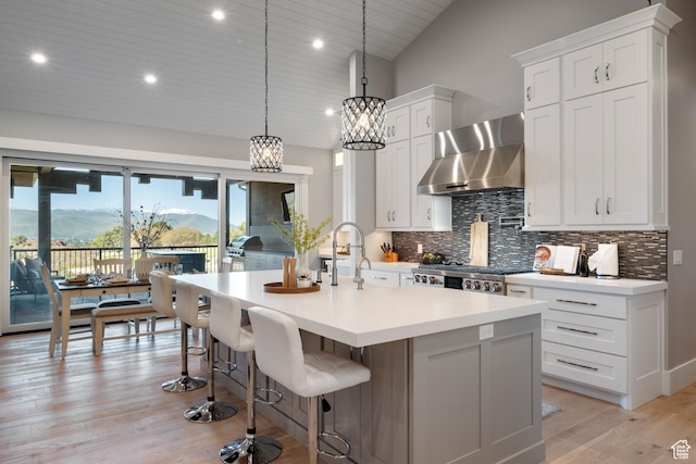 523 N Red Ct, Heber City, UT 84032 - kitchen featuring wall chimney exhaust hood, tasteful backsplash, light countertops, a center island with sink, and light wood-style flooring