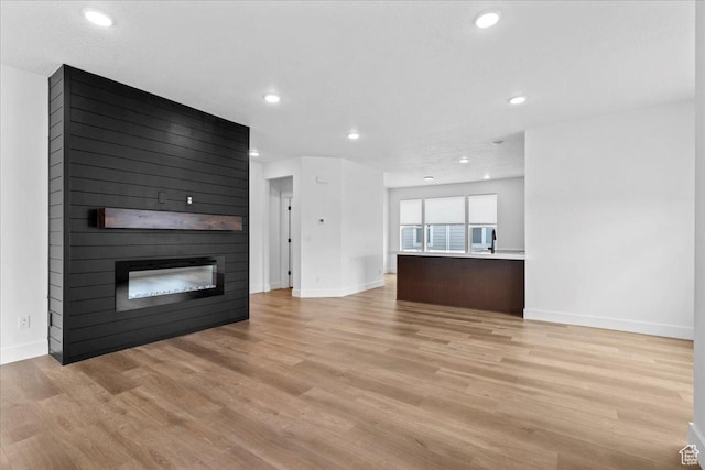 3466 S Peebles Ct E, South Salt Lake, UT 84115 - unfurnished living room with a large fireplace, light wood finished floors, baseboards, recessed lighting, and a sink