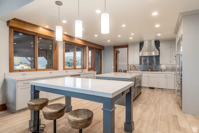 7778 N Greenfield Dr, Park City, UT 84098 - kitchen featuring wall chimney exhaust hood, an island with sink, decorative backsplash, light wood-style floors, and light countertops