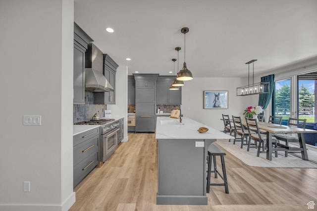 336 Big Meadow Dr, Kamas, UT 84036 - kitchen featuring high end stainless steel range, wall chimney exhaust hood, light wood finished floors, a kitchen breakfast bar, and backsplash
