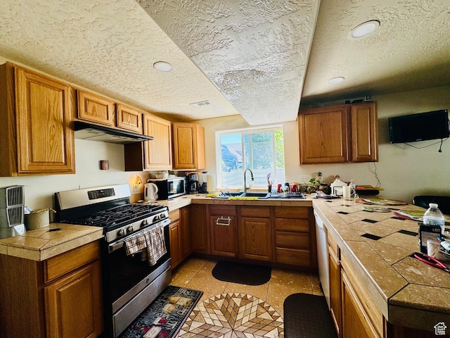 2552 W 2025 N, Clinton, UT 84015 - kitchen with stainless steel appliances, a sink, under cabinet range hood, a textured ceiling, and brown cabinets