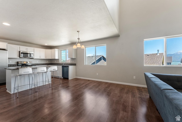 2956 S Willow Creek Dr, Saratoga Springs, UT 84045 - kitchen with stainless steel appliances, open floor plan, white cabinetry, dark countertops, and baseboards