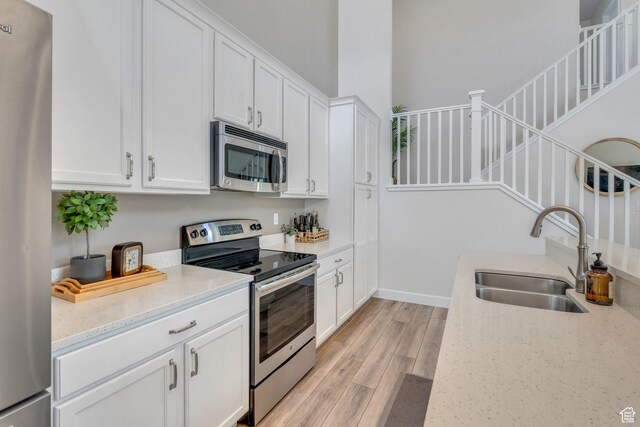 10394 S Crow Wing Dr, South Jordan, UT 84009 - kitchen with stainless steel appliances, a sink, light wood finished floors, white cabinets, and light stone counters