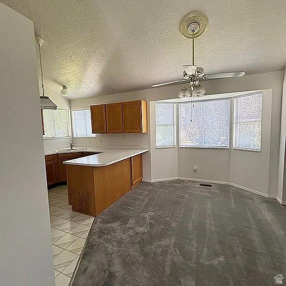 4853 W Ticklegrass Rd, West Jordan, UT 84081 - kitchen featuring a textured ceiling, a sink, a peninsula, brown cabinets, and a ceiling fan