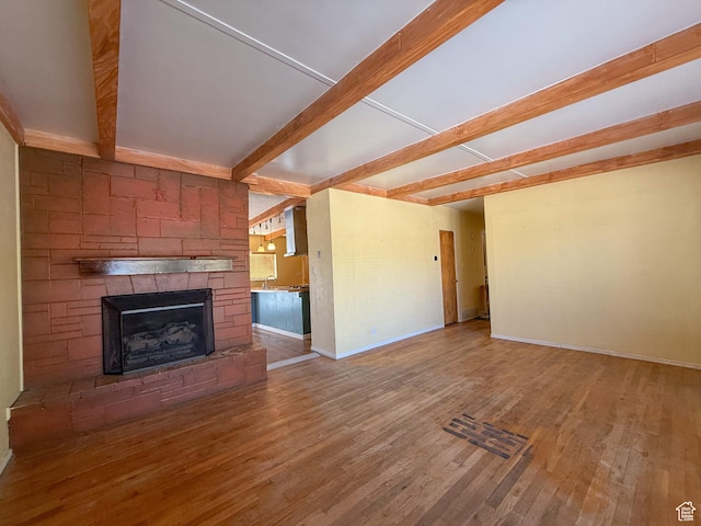 775 N 500 E, Price, UT 84501 - unfurnished living room with beamed ceiling, wood finished floors, a stone fireplace, baseboards, and a sink