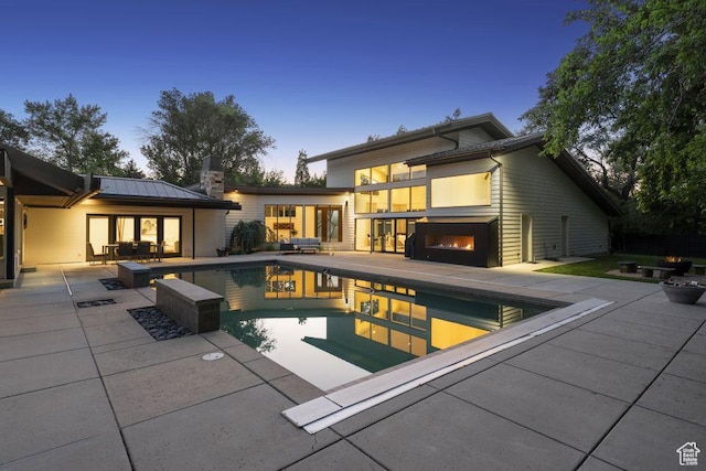 2067 E Pheasant Cir, Holladay, UT 84121 - back of house at dusk featuring a patio, an outdoor pool, and a lit fireplace