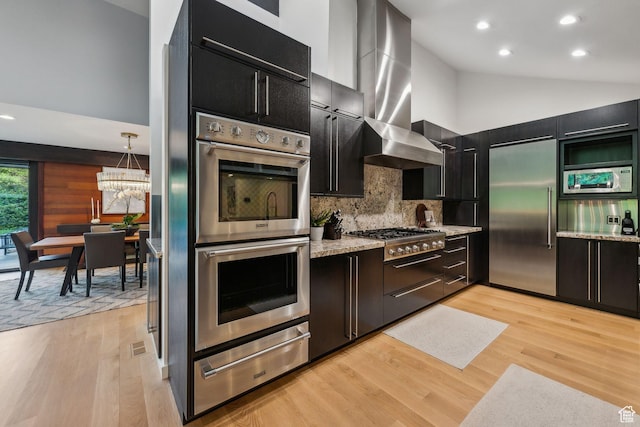 2067 E Pheasant Cir, Holladay, UT 84121 - kitchen featuring stainless steel appliances, a warming drawer, dark cabinetry, wall chimney range hood, and light wood finished floors