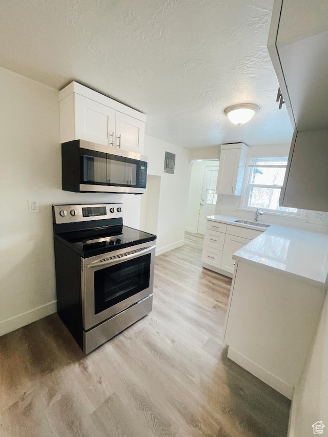 751 E Scott Ave, Millcreek, UT 84106 - kitchen with stainless steel appliances, baseboards, white cabinets, light wood finished floors, and a textured ceiling