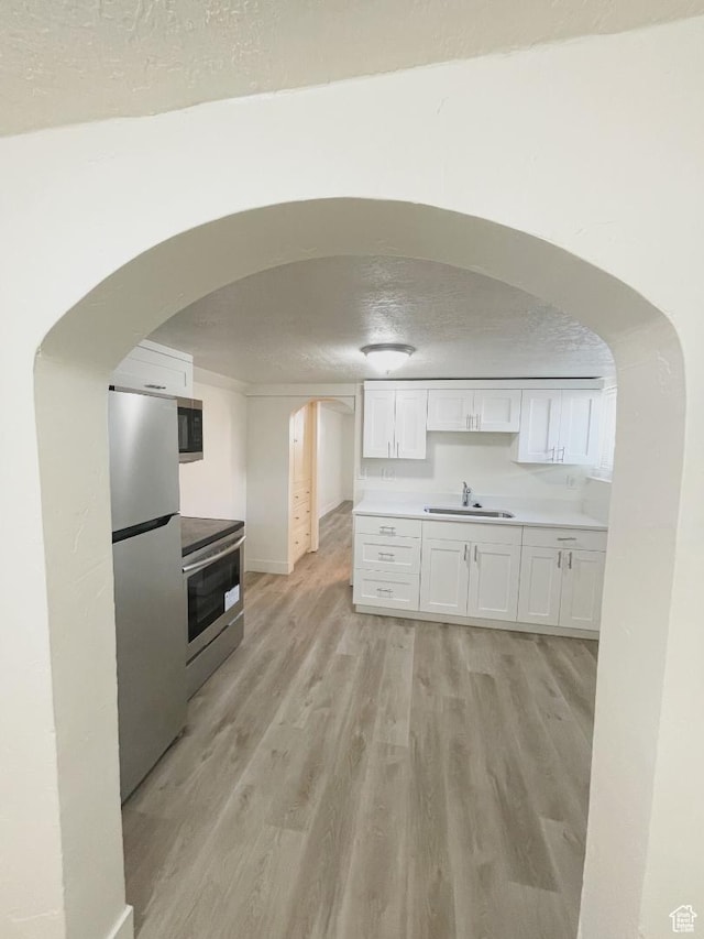 751 E Scott Ave, Millcreek, UT 84106 - kitchen with appliances with stainless steel finishes, a sink, light wood-style flooring, white cabinetry, and arched walkways