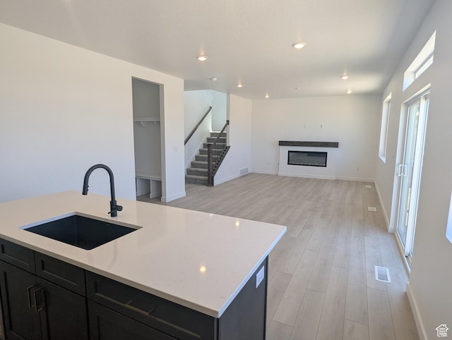 737 N Plainsman Dr Unit 108, Spanish Fork, UT 84660 - kitchen featuring light wood-style floors, dark cabinetry, a glass covered fireplace, recessed lighting, and light stone countertops