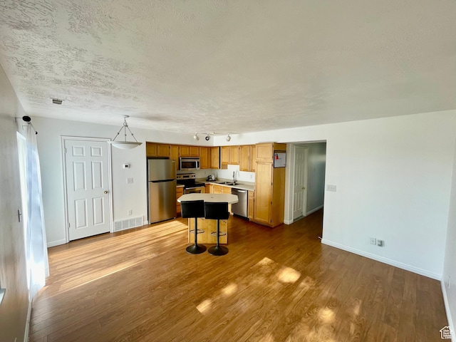 6939 S Florentine Way, West Jordan, UT 84084 - kitchen featuring appliances with stainless steel finishes, light countertops, wood finished floors, a textured ceiling, and a kitchen island