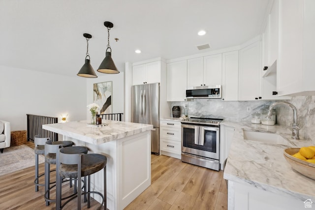 984 Uri Ln Unit 3, Midway, UT 84049 - kitchen featuring appliances with stainless steel finishes, a sink, a center island, decorative backsplash, and white cabinetry