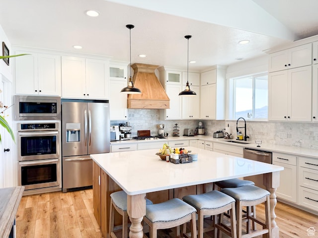 1384 E Abigail Ln, Eagle Mountain, UT 84005 - kitchen with appliances with stainless steel finishes, a sink, custom exhaust hood, a breakfast bar, and light wood-type flooring