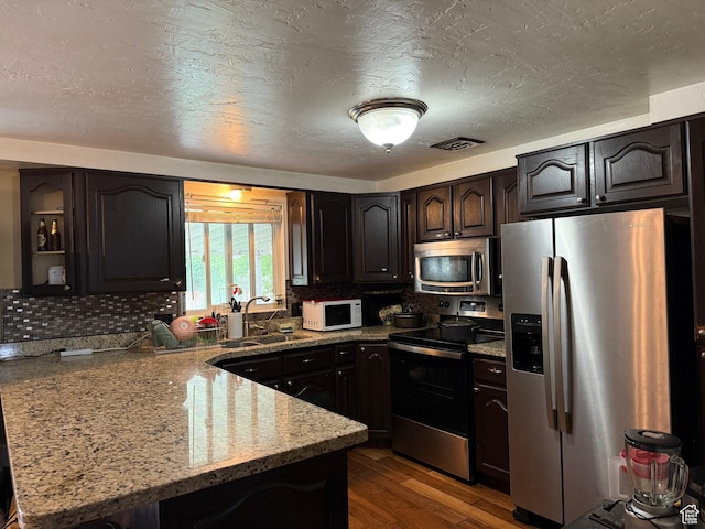 4380 S Perigrine Way, West Valley City, UT 84120 - kitchen with appliances with stainless steel finishes, a peninsula, a sink, tasteful backsplash, and a textured ceiling