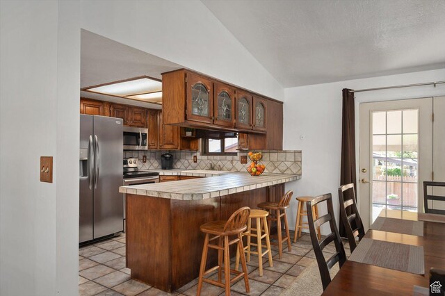 2263 W 4400 S, Roy, UT 84067 - kitchen with appliances with stainless steel finishes, decorative backsplash, a peninsula, vaulted ceiling, and light countertops