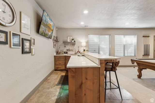 1744 E Burning Oak Dr, Draper, UT 84020 - kitchen with a breakfast bar area, a peninsula, light countertops, baseboards, and brown cabinets