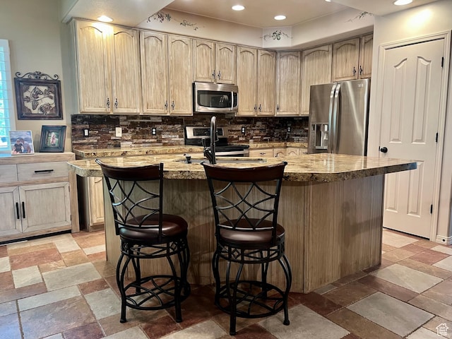 93 E Sweet Berry Ct, Draper, UT 84020 - kitchen with appliances with stainless steel finishes, backsplash, a kitchen island with sink, a kitchen breakfast bar, and light stone finish flooring