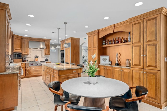 10927 S Lostwood Dr, Sandy, UT 84092 - kitchen featuring wall chimney range hood, appliances with stainless steel finishes, light tile patterned flooring, a center island, and brown cabinets