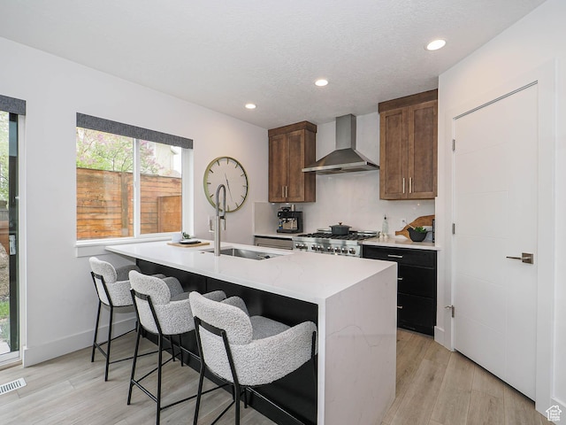 4535 S Bleecker Pl, Millcreek, UT 84117 - kitchen with wall chimney range hood, stove, light wood-style floors, an island with sink, and recessed lighting