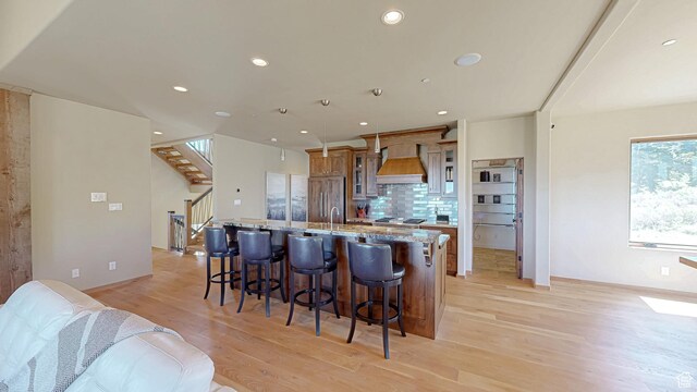 22677 E Snowbird Dr Unit 47, Spanish Fork, UT 84660 - kitchen with premium range hood, light wood finished floors, a center island with sink, a breakfast bar area, and decorative backsplash