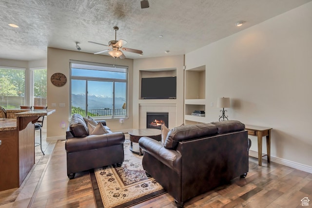 1804 E Longbranch Ct, Draper Ut Cnty, UT 84020 - living room featuring light wood finished floors, a tile fireplace, a textured ceiling, baseboards, and recessed lighting