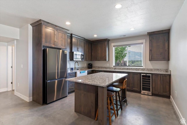 1243 Kotter Dr, Brigham City, UT 84302 - kitchen featuring stainless steel appliances, beverage cooler, finished concrete flooring, baseboards, and a kitchen breakfast bar