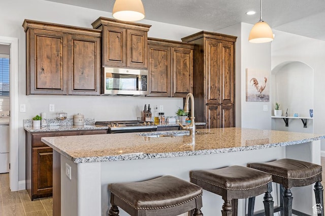 2738 W 270 N, Hurricane, UT 84737 - kitchen featuring stainless steel microwave, a sink, a kitchen breakfast bar, light stone counters, and decorative light fixtures