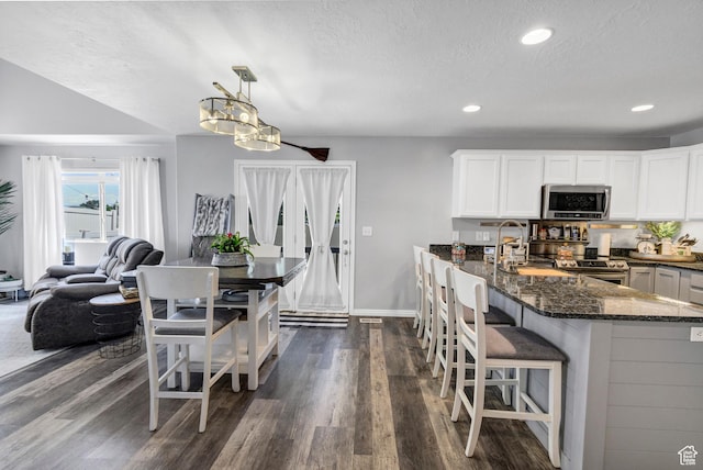 1038 N Plaza Dr, Richfield, UT 84701 - kitchen with stainless steel appliances, dark stone counters, dark wood finished floors, a breakfast bar, and white cabinetry