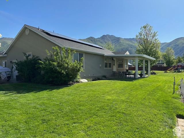 2025 E Skyline Dr, South Ogden, UT 84403 - back of house with a patio area, a mountain view, roof mounted solar panels, a lawn, and stucco siding