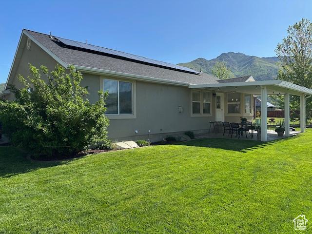 2025 E Skyline Dr, South Ogden, UT 84403 - rear view of property featuring roof mounted solar panels, stucco siding, a patio, and a lawn