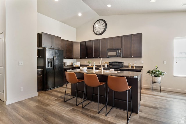 1135 Surrey Dr, North Salt Lake, UT 84054 - kitchen featuring black appliances, dark countertops, high vaulted ceiling, a breakfast bar area, and a kitchen island with sink