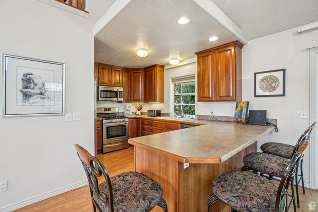 4538 Cottage Grove Ln, Murray, UT 84107 - kitchen with stainless steel appliances, a textured ceiling, light wood-type flooring, a peninsula, and a breakfast bar