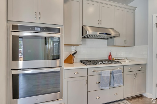 5058 W Blythswood Ln S, Herriman, UT 84096 - kitchen featuring under cabinet range hood, appliances with stainless steel finishes, light countertops, decorative backsplash, and gray cabinets
