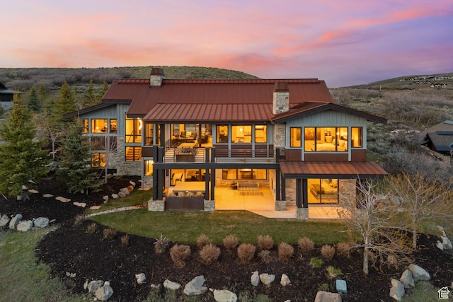 8982 N Mountain Crest Rd, Park City, UT 84098 - back of house at dusk with stone siding, a chimney, and a patio area