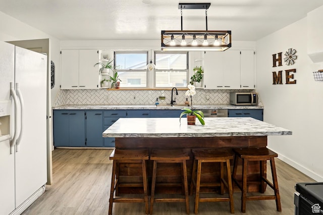 2411 S D Ave E, Ogden, UT 84401 - kitchen featuring white fridge with ice dispenser, stainless steel microwave, blue cabinets, a sink, and tasteful backsplash