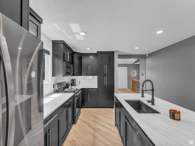 10685 S Superior Cir E, Sandy, UT 84094 - kitchen with appliances with stainless steel finishes, a sink, light stone counters, light wood finished floors, and dark cabinetry