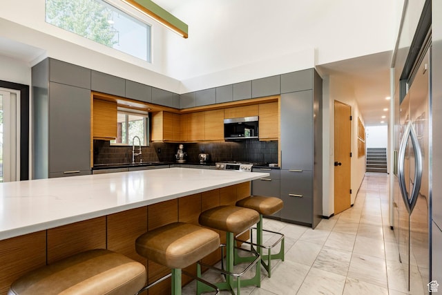 1983 W Ranch Rd, Farmington, UT 84025 - kitchen with appliances with stainless steel finishes, a breakfast bar, gray cabinetry, backsplash, and a towering ceiling