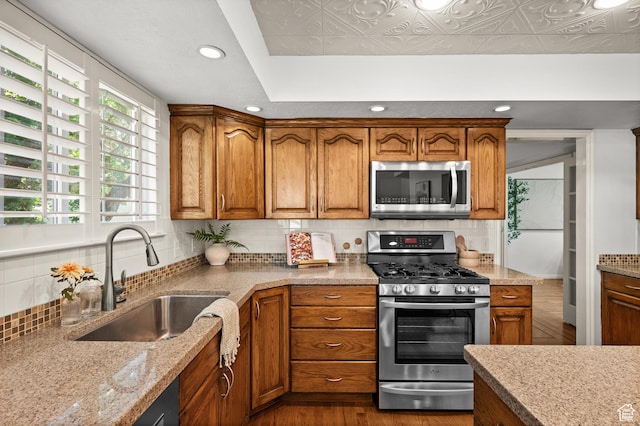 12563 S Bear Castle Cv, Draper, UT 84020 - kitchen with stainless steel appliances, a sink, decorative backsplash, brown cabinets, and recessed lighting