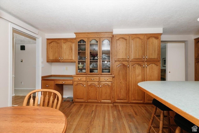 310 E Valley View Dr, Preston, ID 83263 - kitchen featuring brown cabinetry, light wood-style floors, a textured ceiling, glass insert cabinets, and light countertops